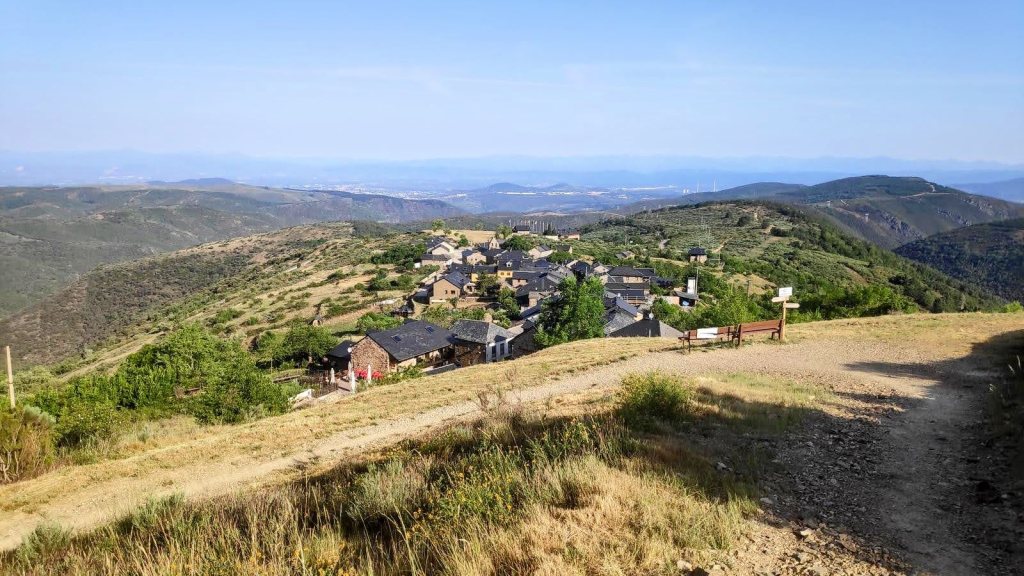 Vista panorámica de la localidad El Acebo de San Miguel, situada en las montañas, con casas de piedra y techos oscuros rodeadas de vegetación y montañas.