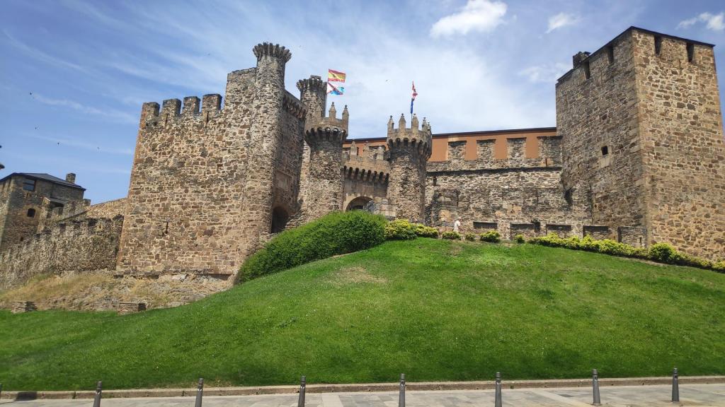 Vista del Castillo de los Templarios en Ponferrada, con sus torres y murallas de piedra, rodeado de un área verde.