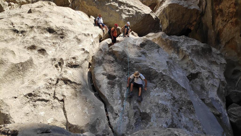 Grupo de personas escalando una roca en la ruta Torrente de Pareis, utilizando cuerdas para descender por una pendiente empinada.