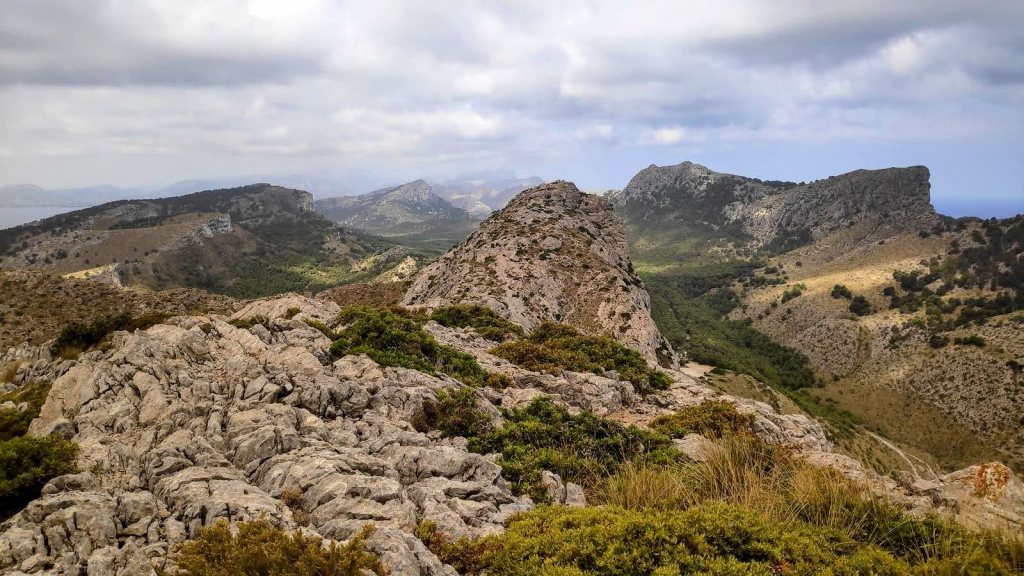 El Fumat y Cala en Gossalba - Caminando por Mallorca Vista panorámica desde la cima de El Fumat, mostrando formaciones rocosas y la vegetación de la Serra de Tramuntana bajo un cielo nublado.