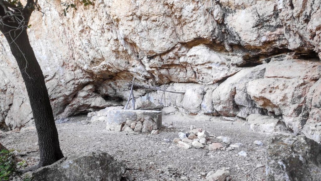 Interior de la Cueva de los Moros en la Comuna de Bunyola, mostrando una cavidad amplia con una mesa redonda en el centro, rodeada de rocas y vegetación.