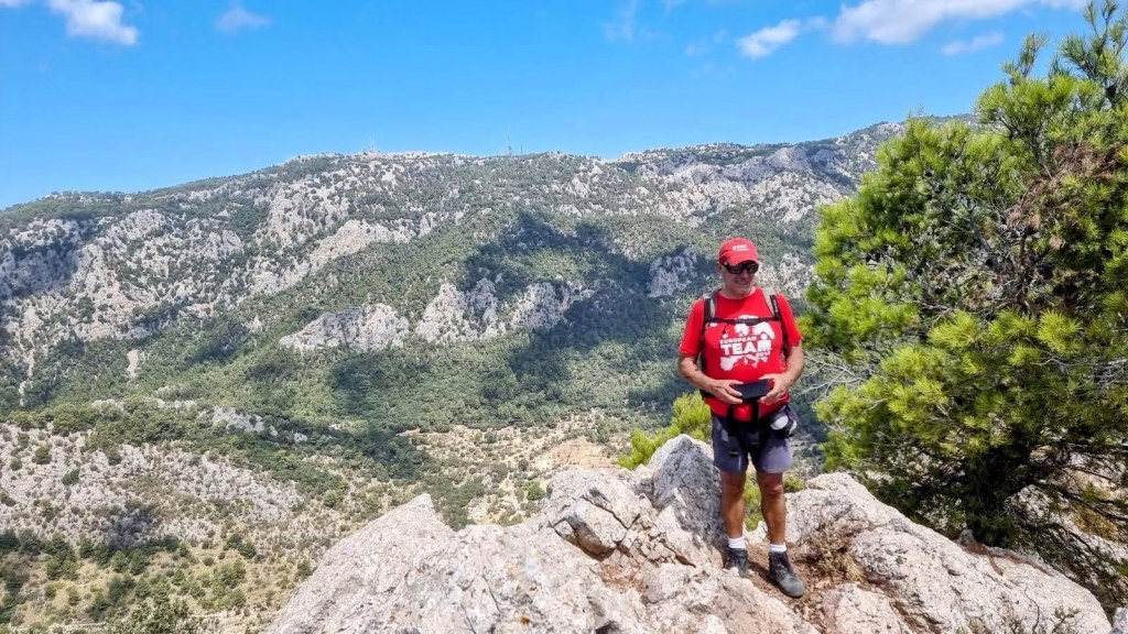 Hombre de pie en una roca con una hermosa vista de montañas y árboles alrededor en la ruta 'Penyal d'Honor por el Pas de Son Creus'.