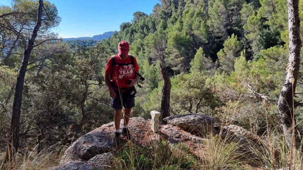 Senderista caminando sobre rocas en un entorno natural con árboles y montañas de fondo durante la ruta Puntals de Planicia.