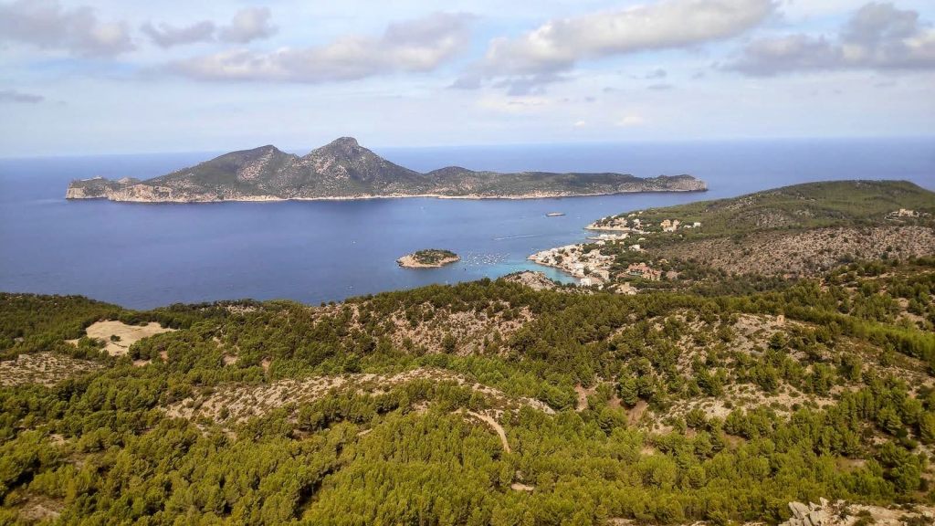 Vista panorámica de la isla Dragonera y el puerto de Sant Elm, rodeada de vegetación y montañas.