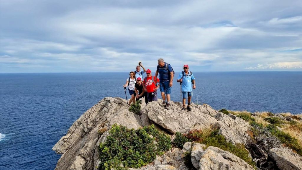 Grupo de excursionistas en la cima de una roca en el Puig de l'Águila, con vistas al mar en el fondo. El cielo está parcialmente nublado.