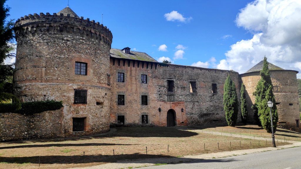 Vista del Castillo de los Marqueses de Villafranca, una construcción histórica con torretas y muros de piedra, rodeado de árboles y un espacio abierto.