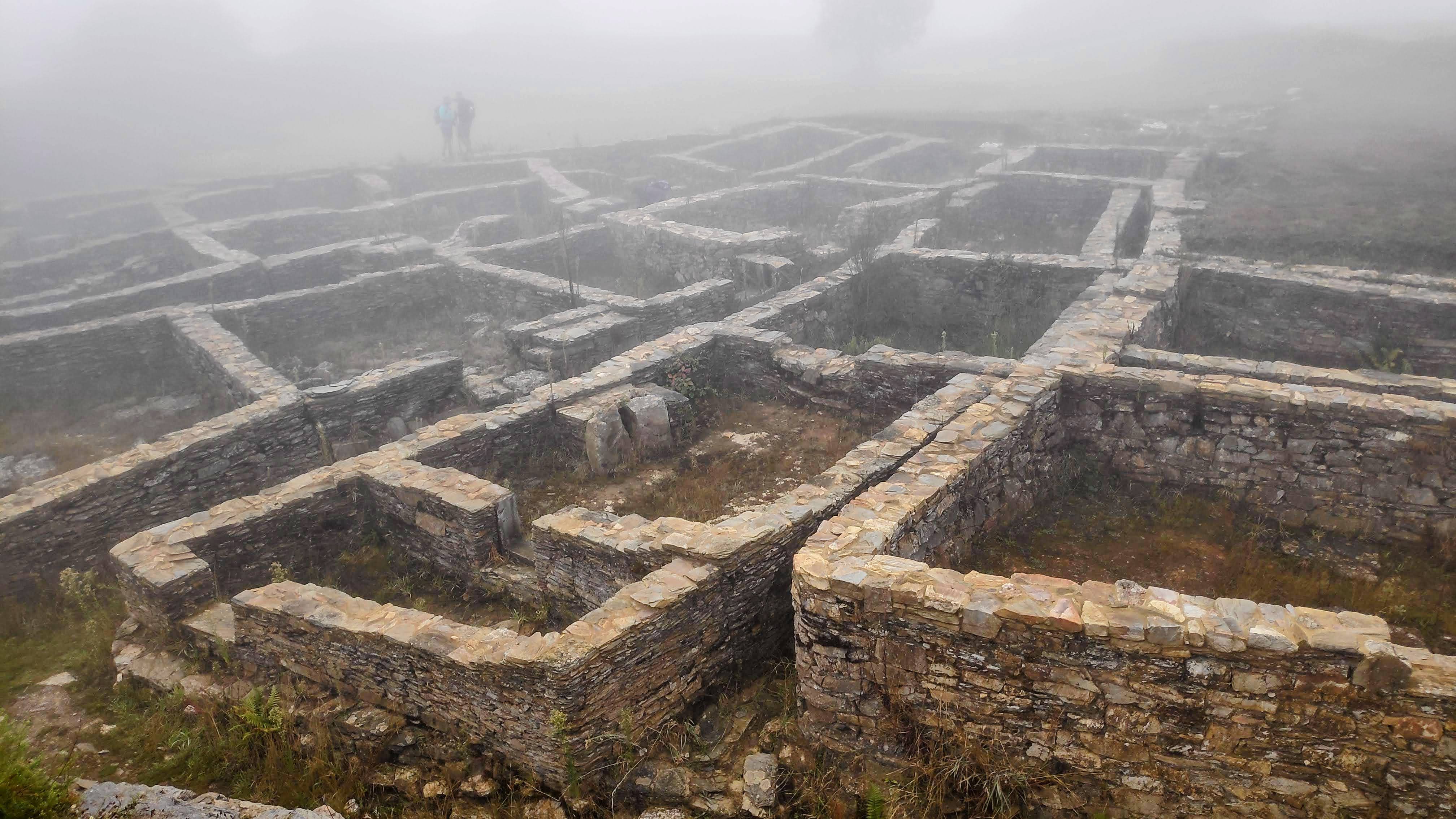 Ruinas de un antiguo asentamiento con estructuras de piedra visibles, rodeadas de niebla.