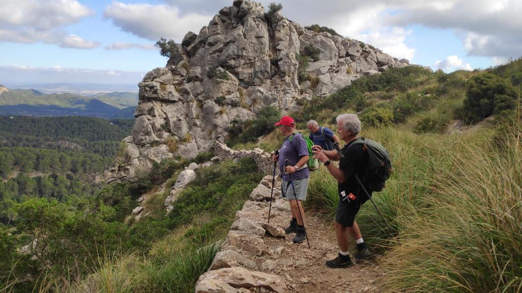 Puig de Galatzó por el Coll d’Estellencs - Caminando por Mallorca Grupo de senderistas en el Pas des Ratxo. con roca prominente y vegetación densa, durante una excursión en la Serra de Tramuntana.