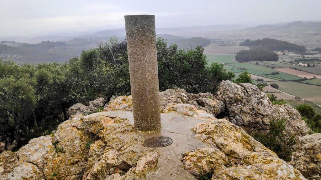 Vista desde la cima del Puig de Sant Nofre con un vértice geodésico y paisaje rural de Mallorca en el fondo.