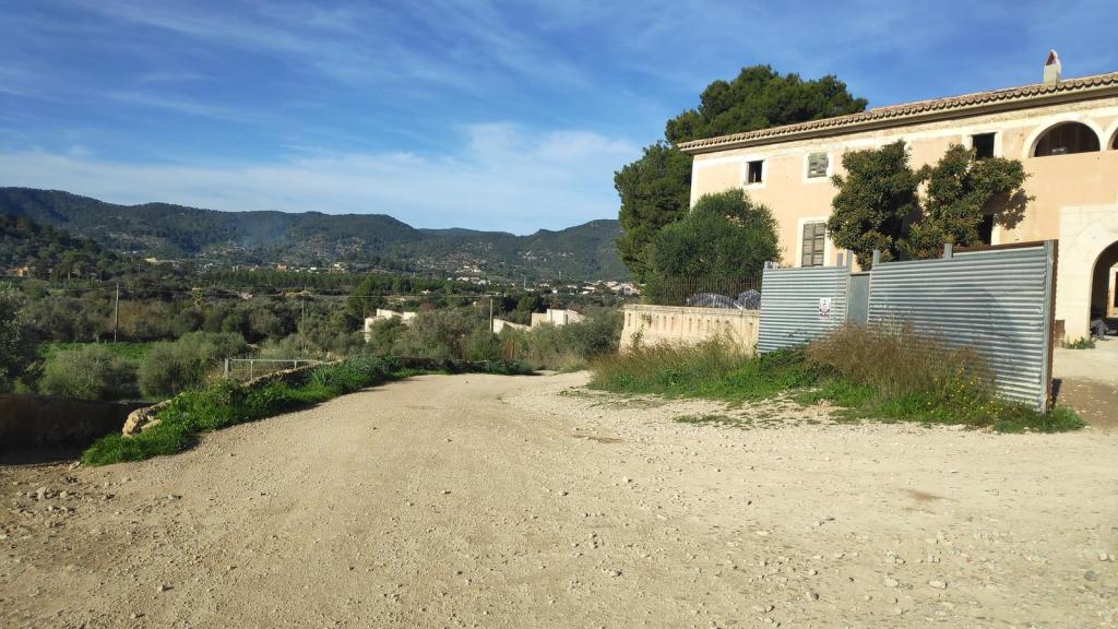 Vista del camino de tierra con un paisaje montañoso al fondo, junto a las casas de Bànyols.