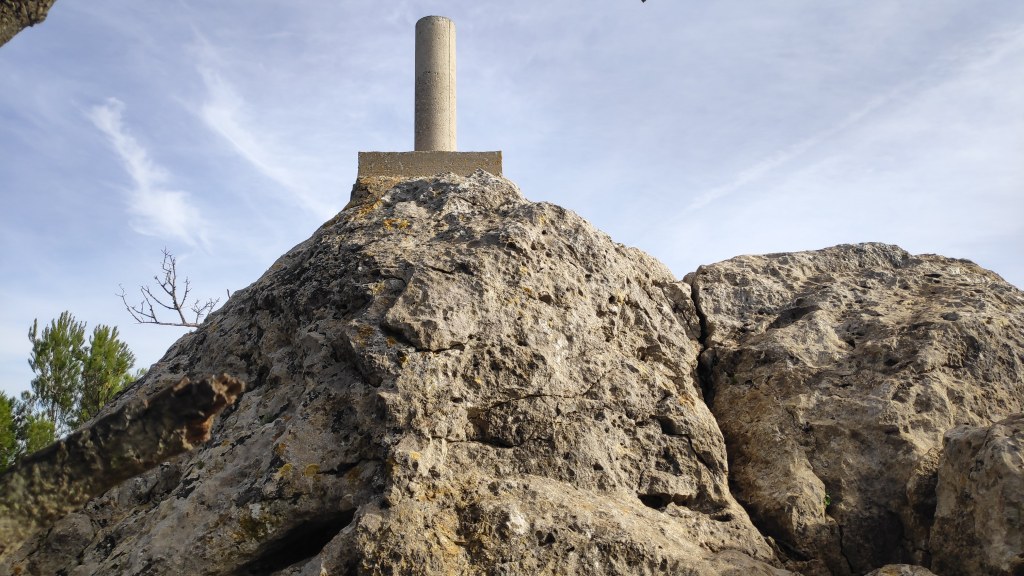 Vista de la cima del Puig de na Bauçana, con un vértice geodésico en la parte superior, rodeada de vegetación y un cielo claro.