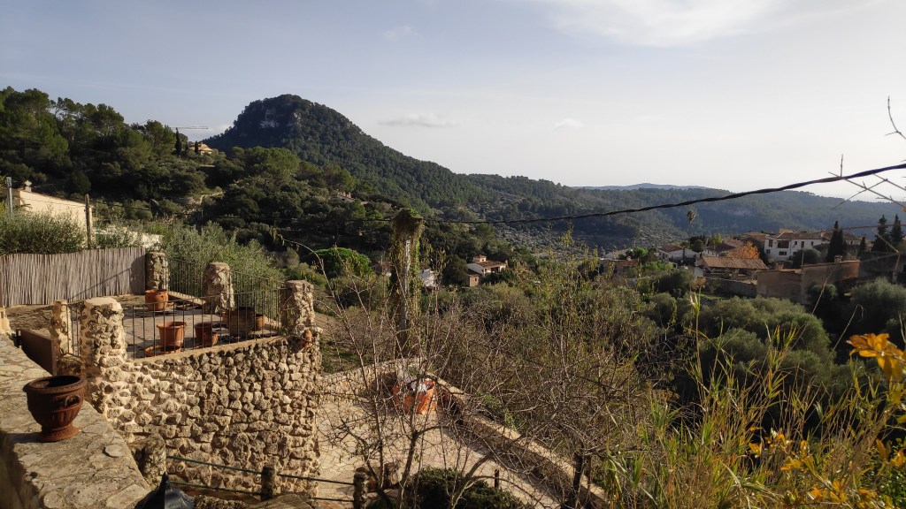 Vista de la montaña Puig de na Bauçana desde una zona elevada en Puigpunyent, con vegetación y casas en el primer plano.