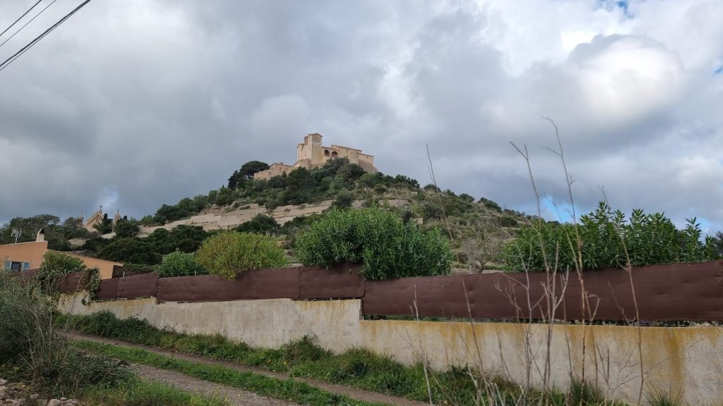 Vista de un castillo en una colina, rodeado de vegetación y un cielo nublado.