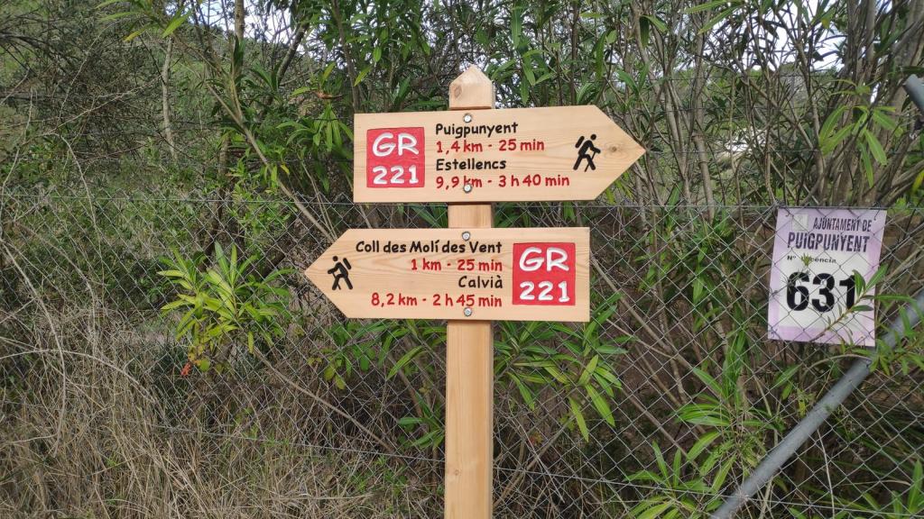 Señalización de ruta GR-221 en Puigpunyent, indicando distancias y tiempos hacia varios destinos.