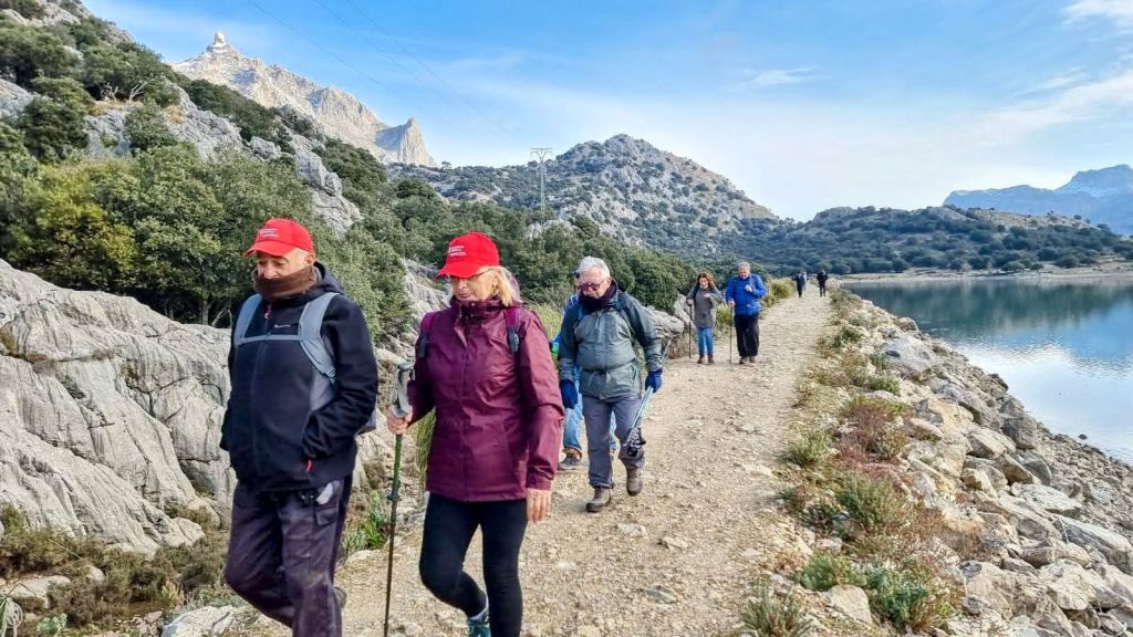 Grupo de personas caminando por un sendero junto al embalse de Cúber, rodeados de montañas y vegetación.