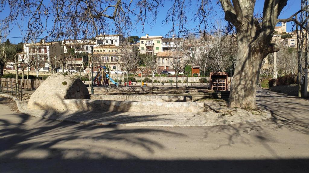 Área de picnic en Selva, con un parque infantil y casas al fondo en un día soleado.