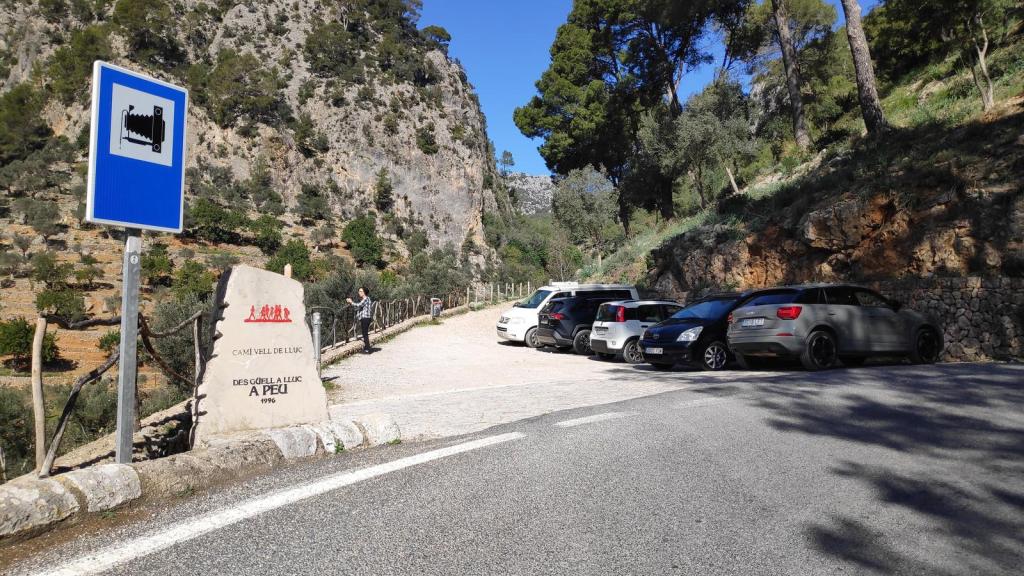 Área de aparcamiento cerca del Camí Vell de Lluc, con varios coches estacionados y un letrero informativo sobre el camino.