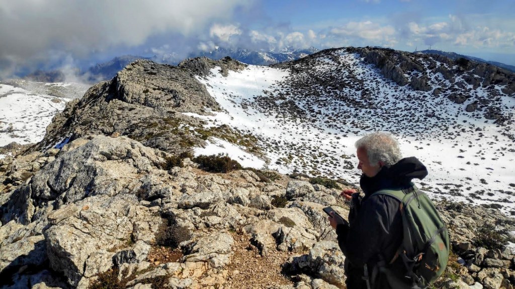 Un senderista en Puig des Teix cubierto de nieve, rodeado de rocas y una vista panorámica de las montañas en el fondo.