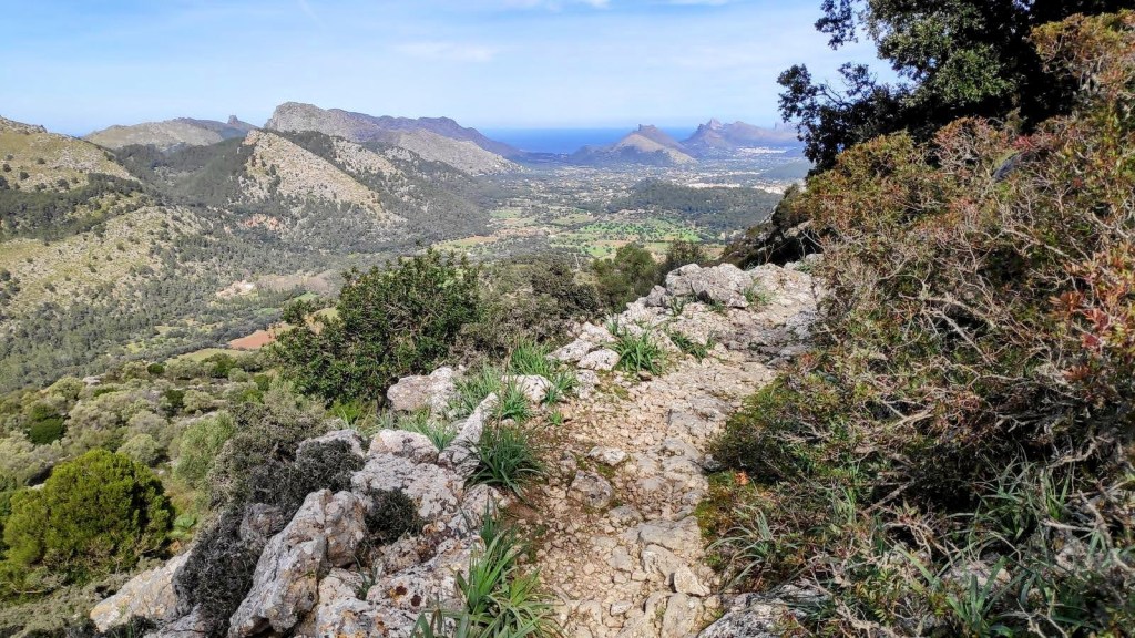 Serra de la Coma por la Regata de la Coma - Caminando por Mallorca Vista panorámica desde un sendero en la Serra de la Coma, mostrando montañas y el valle debajo, con el mar al fondo.