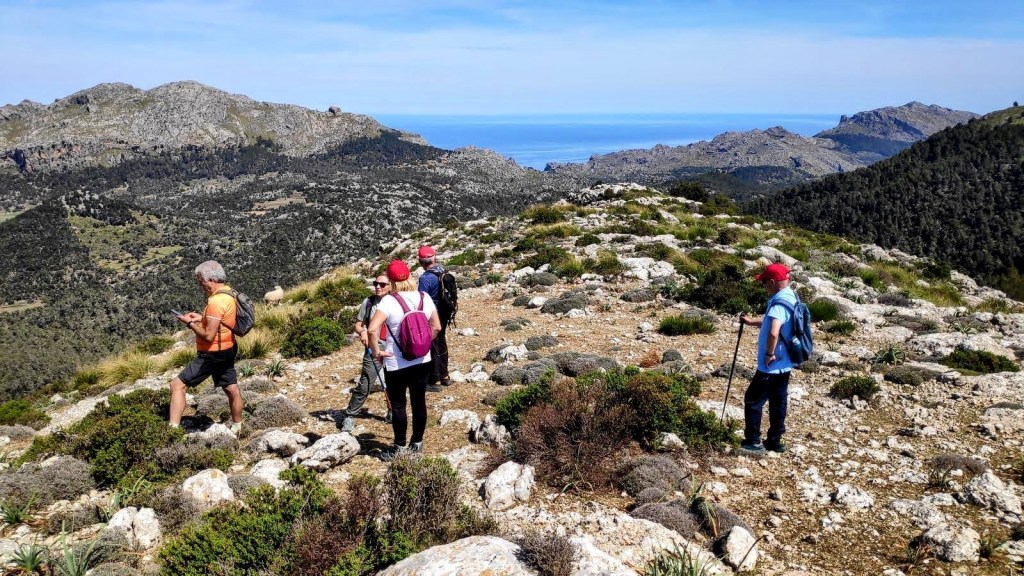 Grupo de personas caminando por la cima de la Moleta de Binifaldó, con vistas panorámicas del valle y el mar en el fondo, durante una ruta de senderismo.