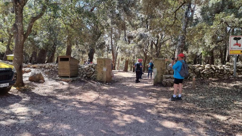 Grupo de personas en un sendero del bosque cerca de una entrada al Área Recreativa Menut I, con un vehículo estacionado y una zona de descanso al fondo.