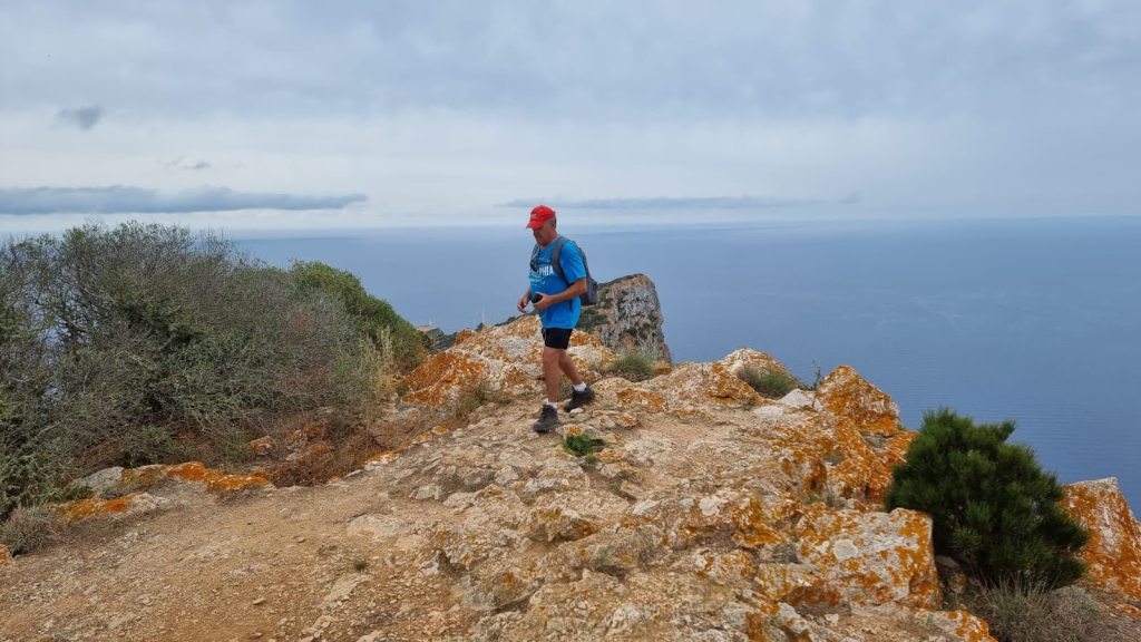 Un senderista camina por el Cap des Llebeig con vistas al mar, rodeado de vegetación en el Parque Natural de la Dragonera.