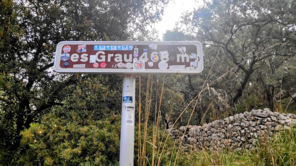 Señal indicativa de la ruta 'es Grau' a 468 metros de altitud, rodeada de vegetación y un paisaje natural.