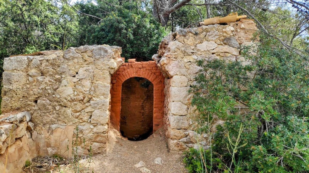 Coll d'Estellencs desde Puigpunyent - Caminando por Mallorca Ruinas de una construcción antigua con un arco de ladrillo, rodeada de vegetación en un entorno natural.
