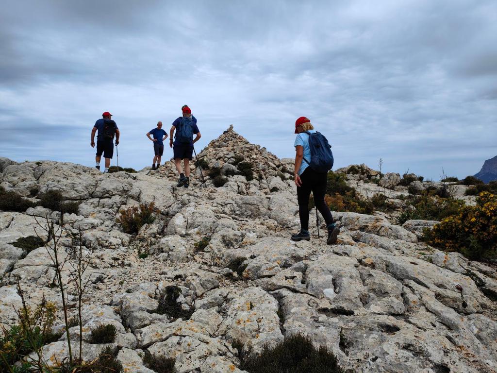 Grupo de excursionistas ascendiendo por un terreno rocoso hacia la cima de Es Cornador Gran, con un hito de piedras visible en el fondo.