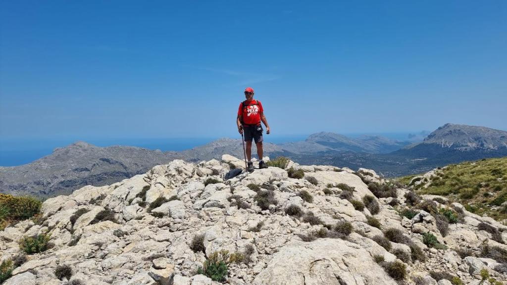 Persona de pie sobre la cima del Puig de sa Mola, con vistas panorámicas al fondo, en un día soleado.