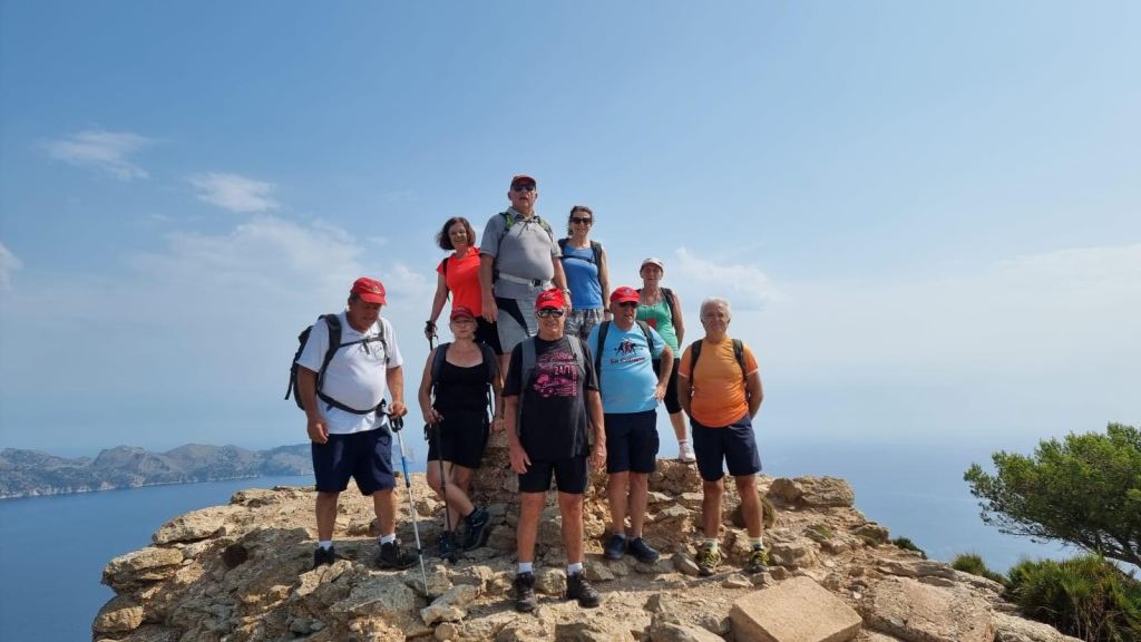 Grupo de senderistas en la cima de la Talaia de Alcudia, disfrutando de vistas panorámicas al mar y las montañas.
