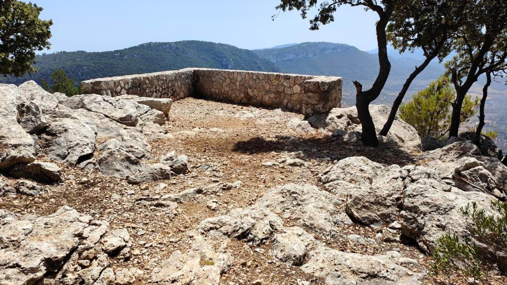 Mirador de piedra con vistas a un paisaje montañoso, rodeado de árboles y rocas.
