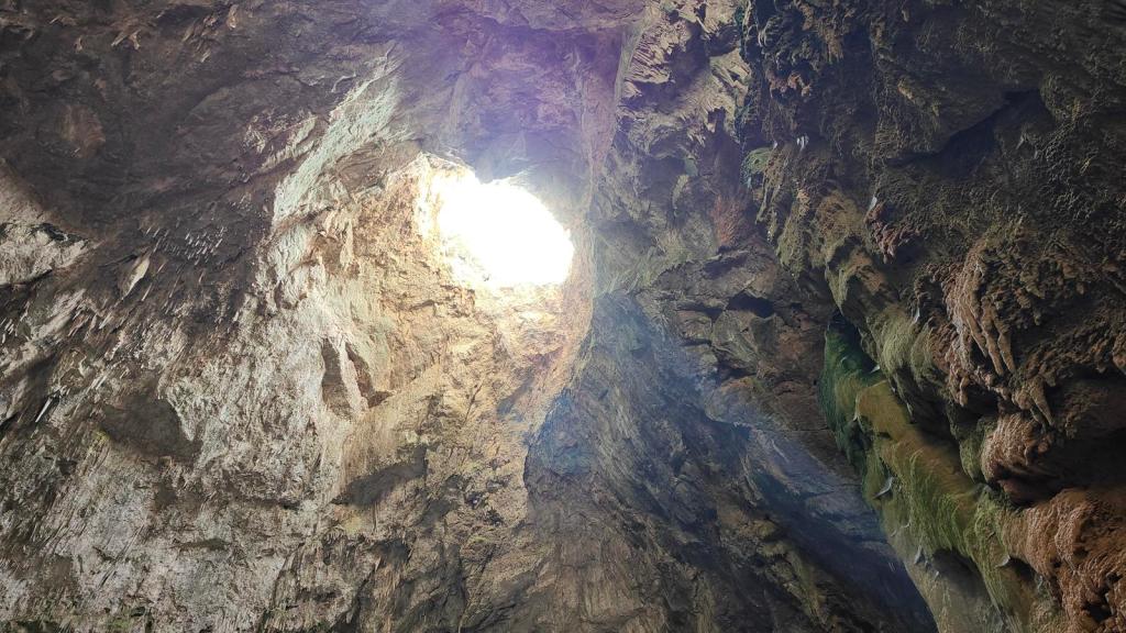 Vista desde el interior del Avenc de Son Pou, con un agujero en el techo por donde entra luz, rodeada de paredes rocosas texturizadas.