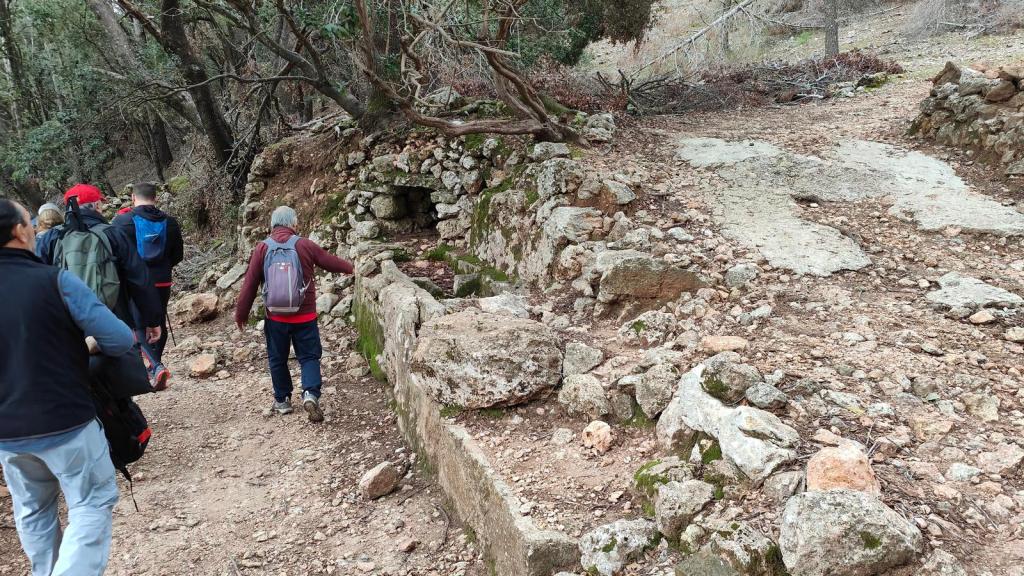 Grupo de personas caminando por un sendero en el campo, con una estructura de piedra en la parte derecha de la imagen.