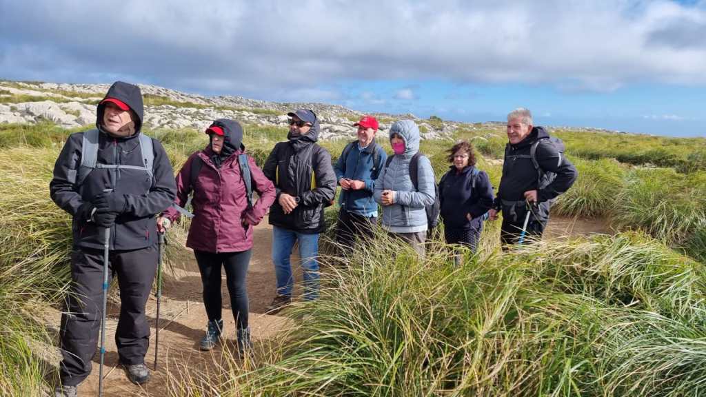 Puig de Massanella - Ruta normal - Caminando por Mallorca Grupo de senderistas en un camino rodeado de hierba alta, visten ropa de abrigo y se preparan para una excursión en la montaña.