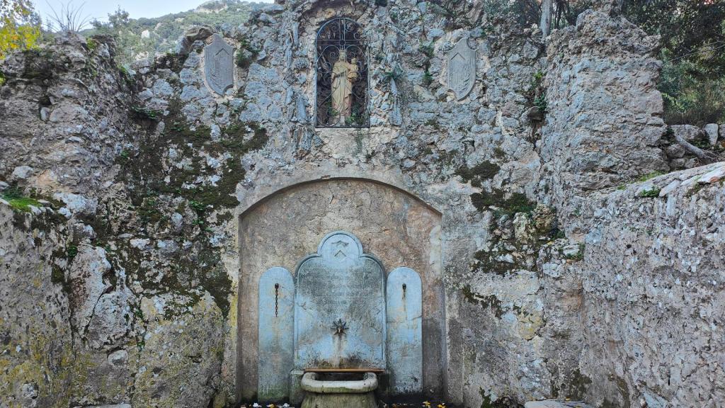 Puig de Galileu por el Pas de la Rebollada - Caminando por Mallorca Antigua fuente situada en un entorno rocoso, con un pequeño altar y una escultura religiosa en la parte superior.