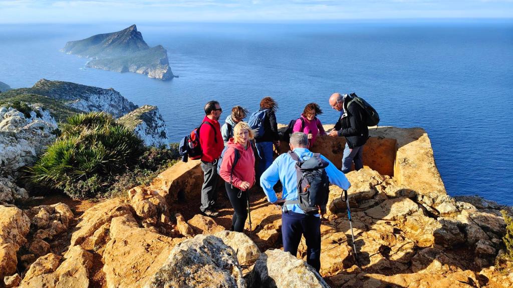 Grupo de excursionistas en un mirador sobre el océano, con vistas a una isla en el horizonte.