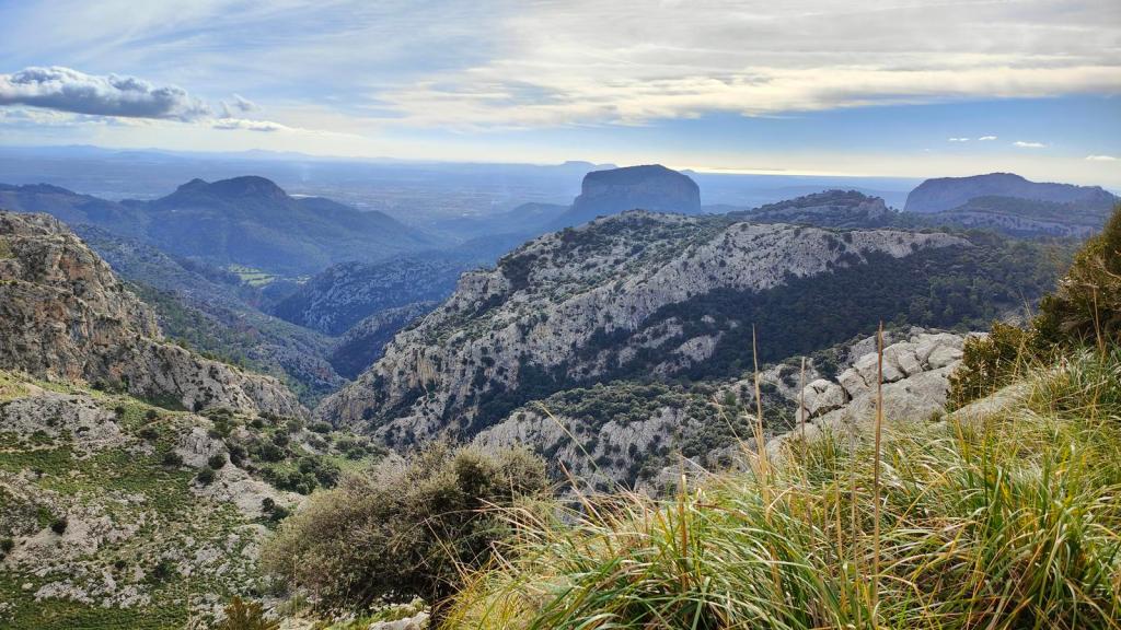 Vista panorámica de las montañas y valles alrededor del embalse de Cúber, con rocas y vegetación en primer plano, bajo un cielo con nubes dispersas.