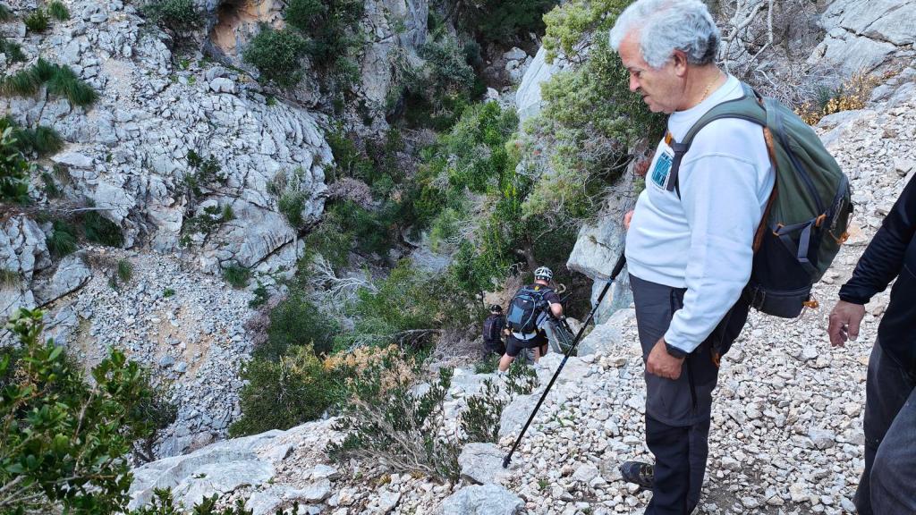 Grupo de excursionistas descendiendo por una ruta rocosa en un paisaje montañoso, con vegetación y rocas alrededor.