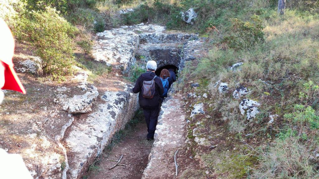 Personas caminando hacia la entrada de una cueva prehistórica en un entorno natural