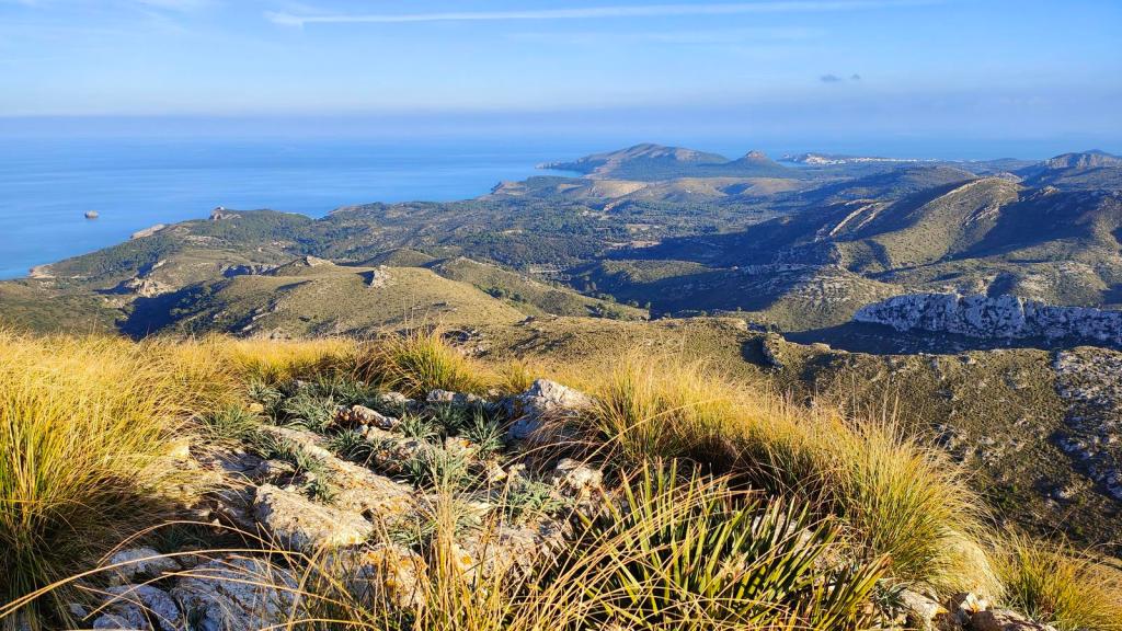 Vista panorámica desde la cima del Puig des Porrassar, mostrando un paisaje montañoso con vegetación y el mar en el fondo.