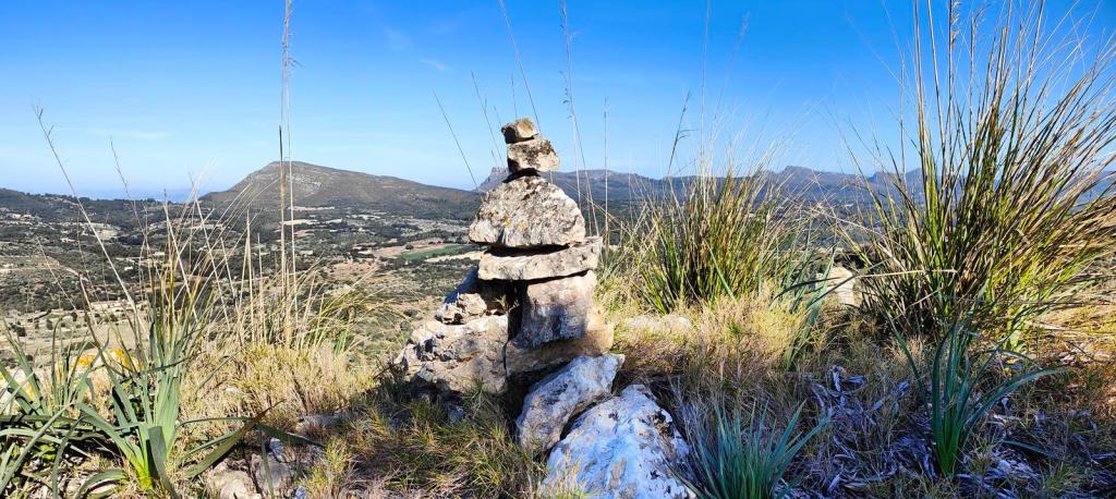 Vista panorámica desde el Puig de s'Esquerda, con un hito de piedras en primer plano y vegetación típicamente mediterránea en la ladera.
