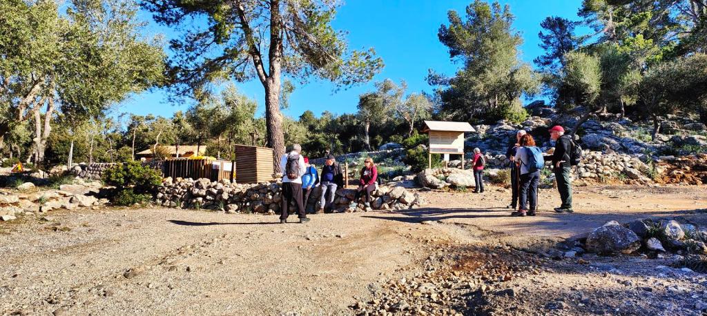 Es Pixarells desde Lluc - Caminando por Mallorca Grupo de personas en un sendero de montaña, con vegetación de fondo y un área recreativa visible.