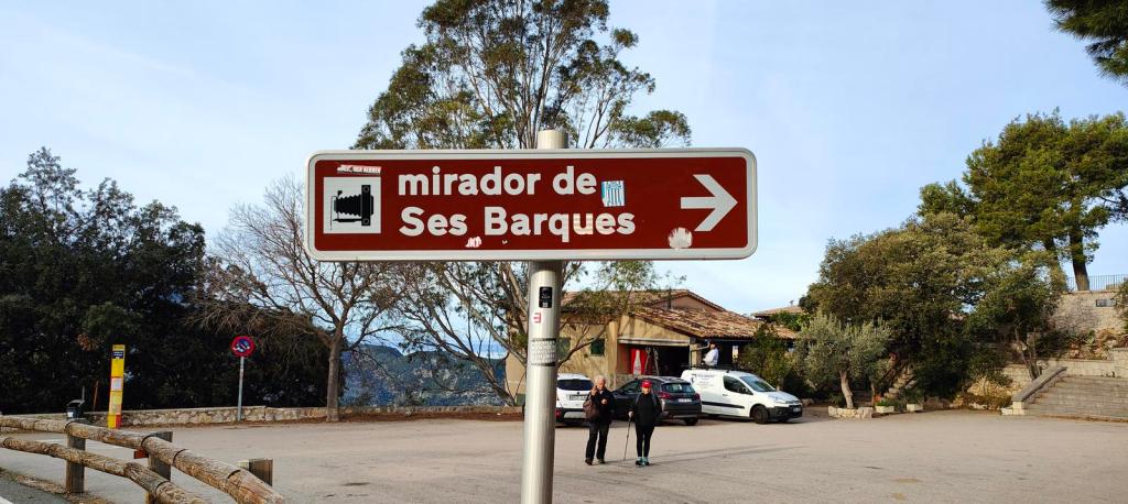 Señal indicativa hacia el Mirador de ses Barques, con un paisaje de fondo que incluye árboles y una edificación.