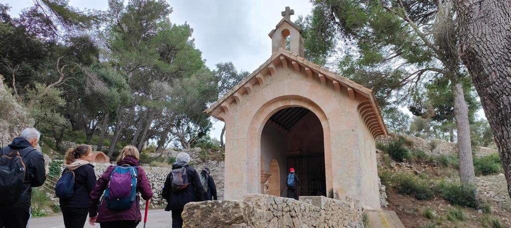 Grupo de personas caminando hacia la capilla Sa Capelleta en un entorno natural de bosque.
