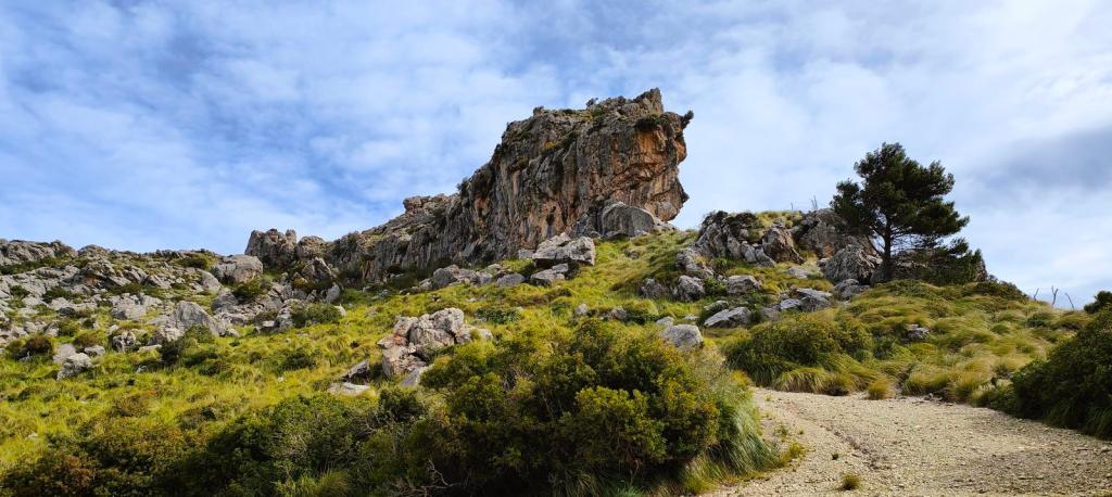 Sierra de Pedruixella - Caminando por Mallorca Vista de una formación rocosa prominente en un paisaje natural con vegetación verde y un cielo nublado en la ruta 'Sierra de Pedruixella'.