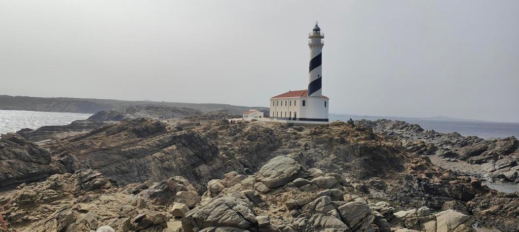 Faro de Favàritx situado en un cabo rocoso, con un cielo nublado y mar al fondo.