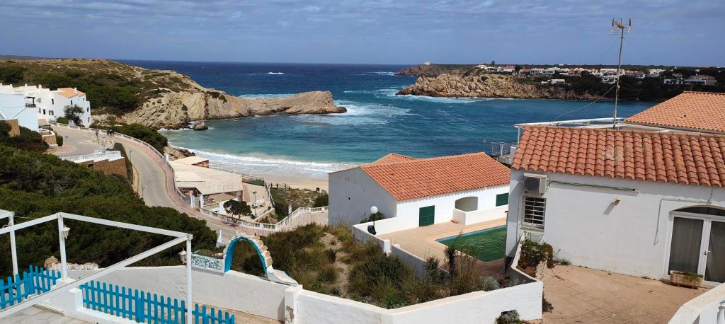 Vista panorámica de S’Arenal d'en Castell, con casas blancas y el mar azul en el fondo, junto a un camino que desciende hacia la playa.