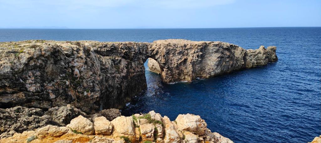 Vista del Pont d'en Gil, un arco de roca natural sobre el mar, rodeado de acantilados y vegetación escasa, en la costa de Menorca.