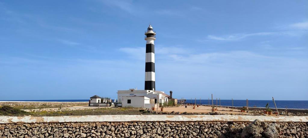 Faro d'Artrutx en Menorca, con su característica torre de rayas blancas y negras, rodeado por el mar y un paisaje llano.